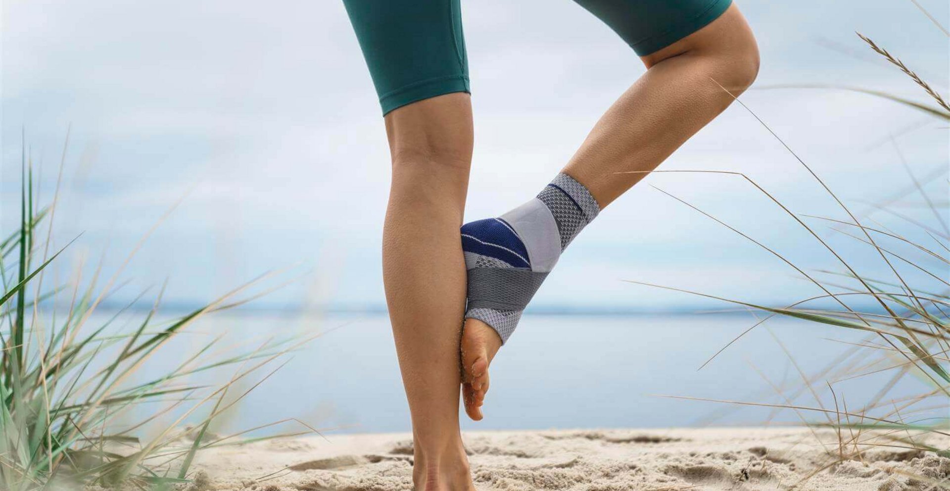 Bildausschnitt einer Frau, die am Strand eine Yoga-Pose einnimmt. Sie trägt die MalleoTrain Sprunggelenkbandage von Bauerfeind, um ihr Sprunggelenk zu stabilisieren.