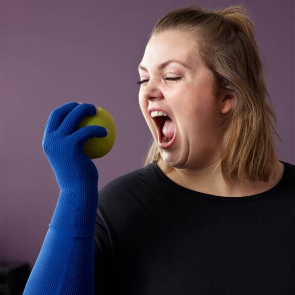 Das Bild zeigt eine Frau mit blauem Kompressionshandschuh und geöffnetem Mund, kurz vor dem Hineinbeißen in einen Apfel. Eine gesunde Ernährung ist bei Lip- oder Lymphödem ein wichtiger Therapiebaustein.
