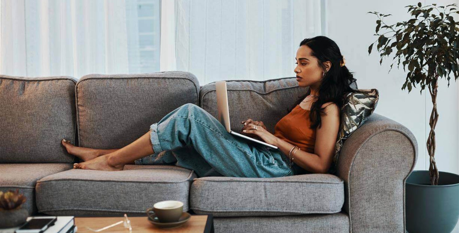 Auf dem Bild sieht man eine Frau, die mit einem Laptop auf dem Sofa liegt. Erfahre, welche gesundheitlichen Folgen Bewegungsmangel haben kann.